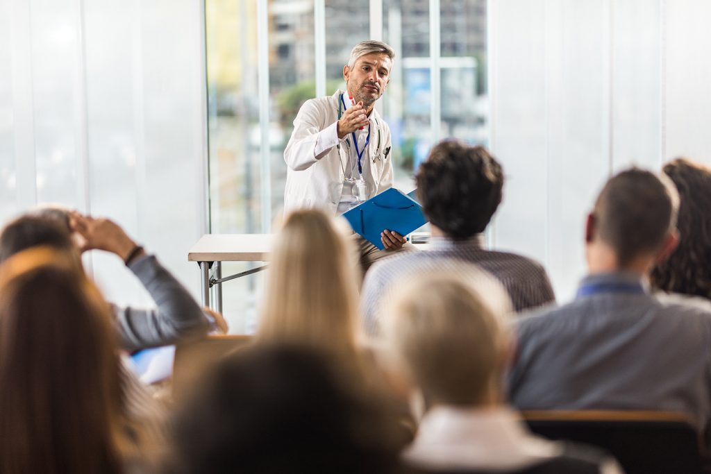 Male doctor talking to large group of people on a seminar in a board room.