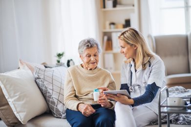 A young health visitor with tablet explaining a senior woman how to take medicine and pills.